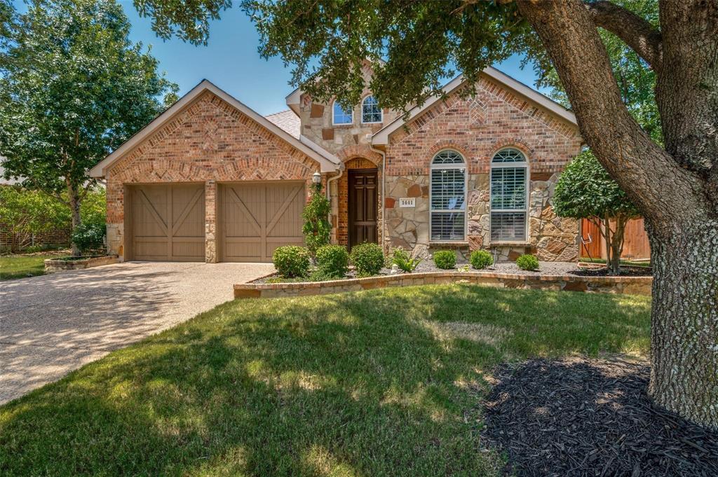 Brick and stone masonry exterior featuring arched windows, double-bay garage with X-brace detailing, and terraced landscaping