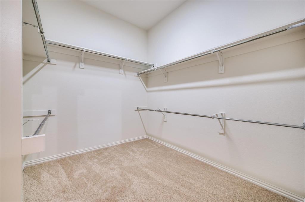 Walk-in closet featuring wall-to-wall carpeting, multiple tiers of metal clothing rods, and white wall shelving