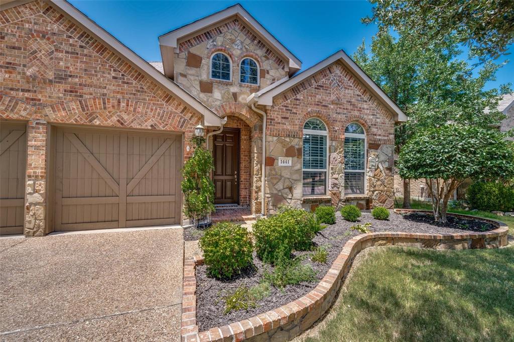 Brick and stone charming exterior featuring arched window detailing, carriage-style garage doors, and a curved masonry garden border