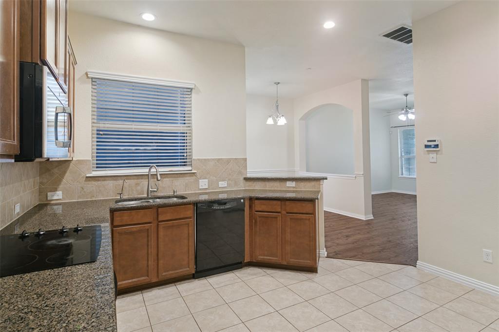 Kitchen featuring stained wood cabinetry, stone-finish countertops, ceramic tile backsplash, integrated black appliance suite, and ceramic tile flooring