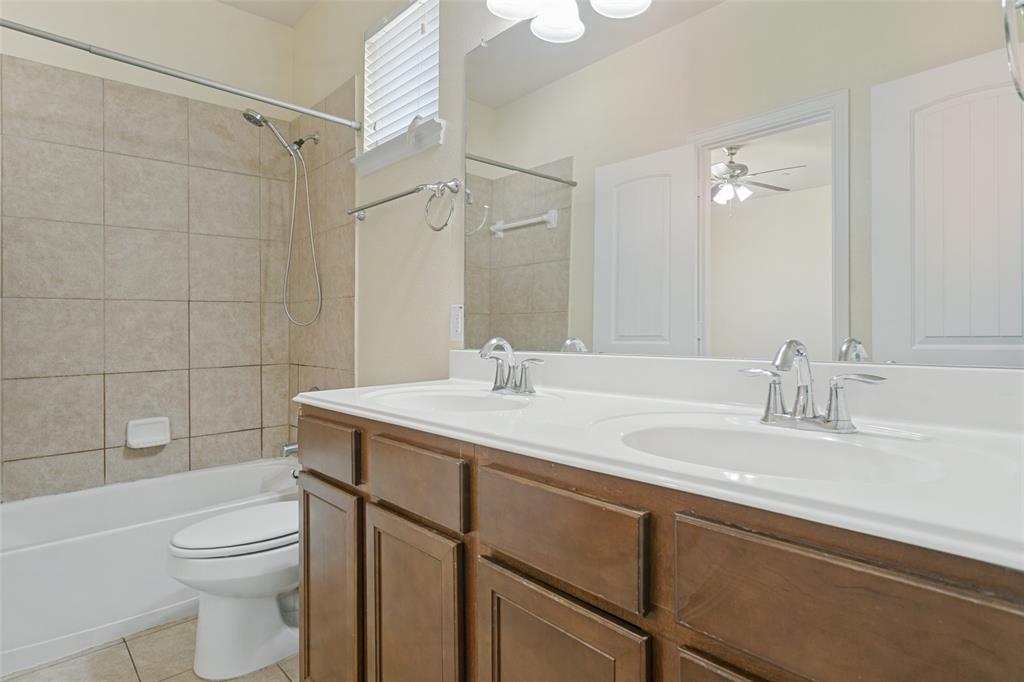 Dual-sink vanity with wood-finish cabinetry, white countertop, oversized wall mirror, and tile-surround shower-tub combination