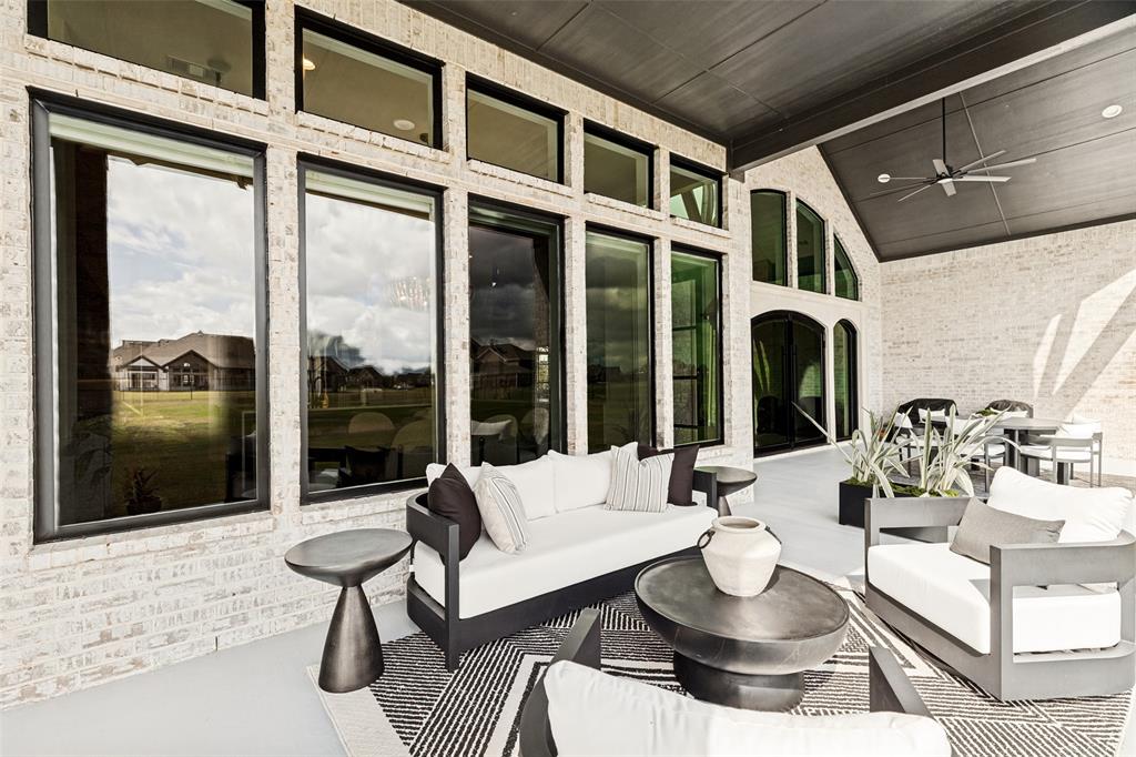 Covered outdoor living area featuring light-colored brick masonry, extensive floor-to-ceiling windows with transom accents, and a dark-finished tongue-and-groove ceiling with a built-in ceiling fan