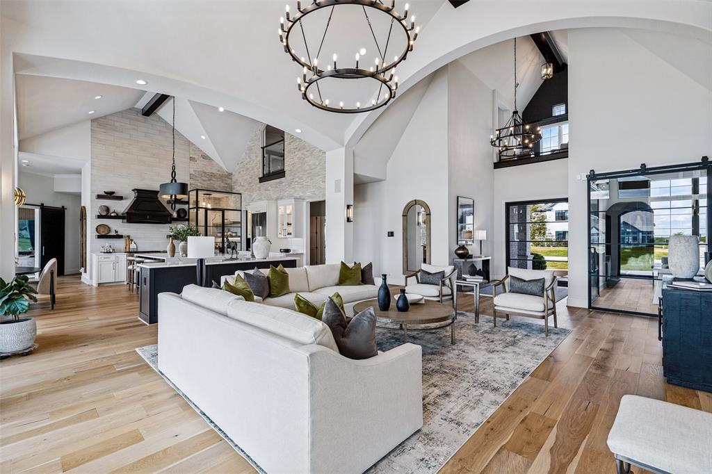 Vaulted ceilings with exposed structural beams, wide-plank wood-finish flooring, floor-to-ceiling stone-clad wall, oversized tiered metal chandeliers, and black-framed sliding glass partition Vaulted ceilings with exposed structural beams, wide-plank wood-finish flooring, floor-to-ceiling stone-clad wall, oversized tiered metal chandeliers, and black-framed sliding glass partition