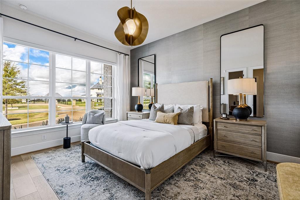 Bedroom featuring wood-finish flooring, a textural gray accent wall, expansive multi-pane windows, and a sculptural gold-tone pendant light fixture