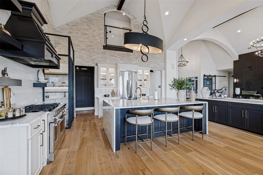 Vaulted ceilings, floor-to-ceiling stone accent wall, oversized central island with waterfall-edge countertop, professional-grade range with custom hood, and wood-finish flooring