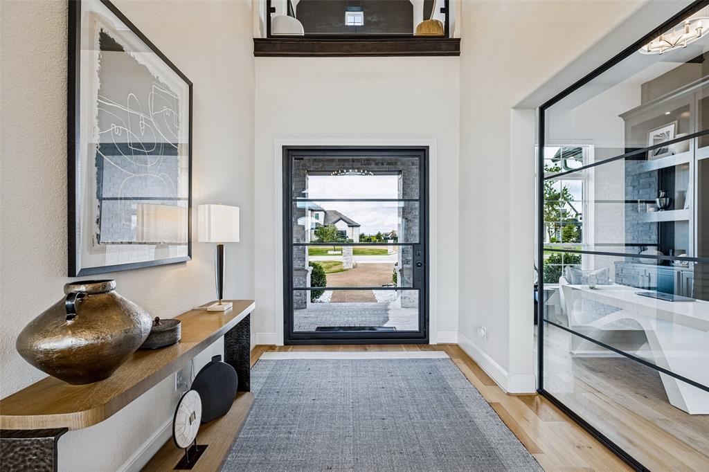 Entryway featuring a double-height ceiling, large-format iron and glass front door, wood-finish flooring, and a floor-to-ceiling glass-paneled partition Entryway featuring a double-height ceiling, large-format iron and glass front door, wood-finish flooring, and a floor-to-ceiling glass-paneled partition