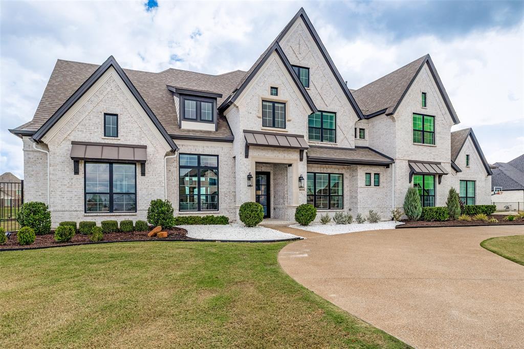 Multi-gabled exterior featuring white brick masonry, dark metal roof accents, multi-pane windows with dark frames, stone-surround entryway, and a concrete aggregate driveway Multi-gabled exterior featuring white brick masonry, dark metal roof accents, multi-pane windows with dark frames, stone-surround entryway, and a concrete aggregate driveway