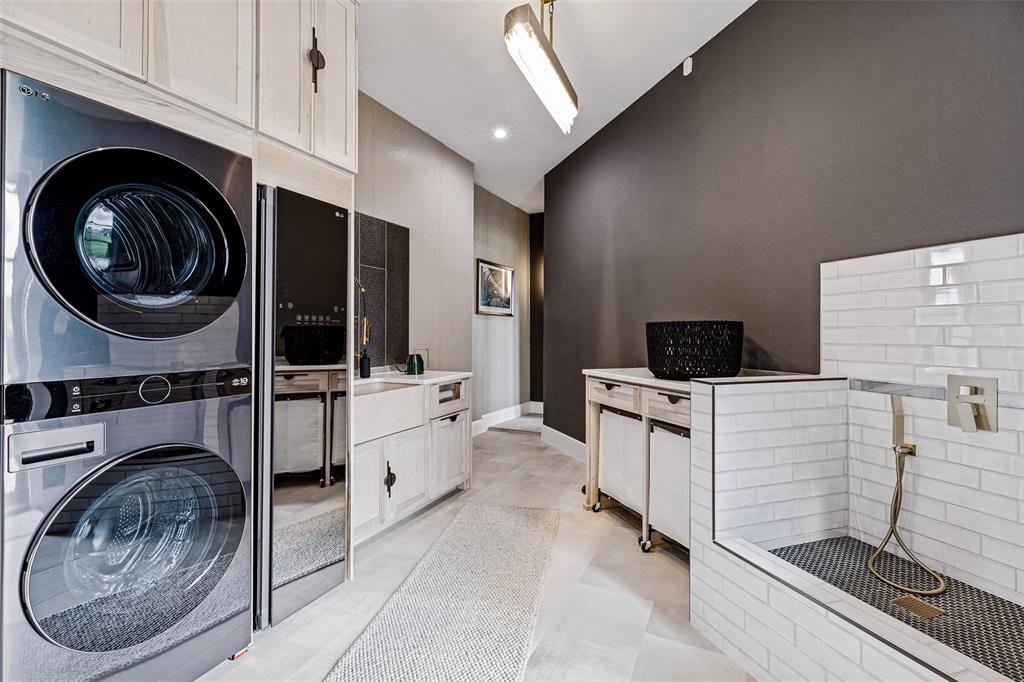 Laundry space featuring custom light-toned cabinetry, farmhouse-style sink, built-in pet wash station with subway tile surround, and stacked appliance configuration