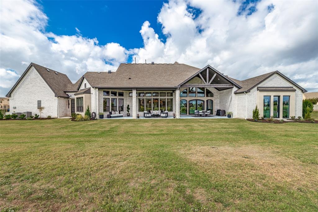 Rear exterior featuring a brick facade, covered patio with vaulted timber-truss ceiling, multi-pane floor-to-ceiling windows, and expansive grass lawn
