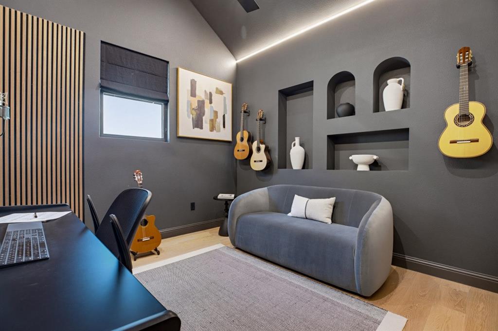 Vaulted ceiling featuring integrated cove lighting, vertical wood-slat accent wall, custom built-in wall niches, and light-tone wood-finish flooring