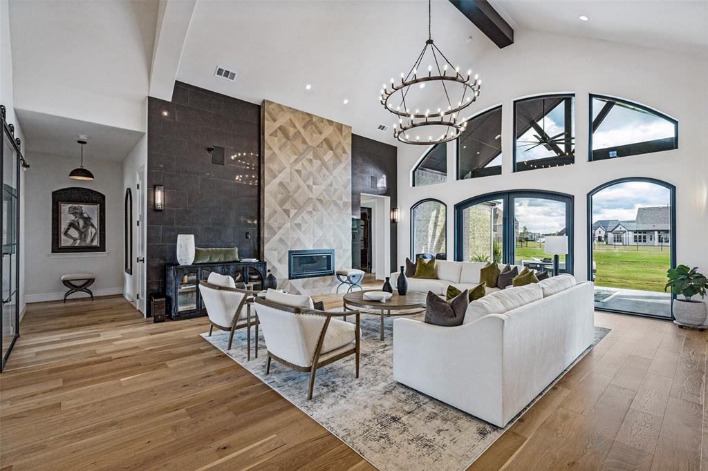 Vaulted ceilings with exposed beams, wood-finish flooring, floor-to-ceiling multi-tone stone fireplace, arched windows, and dual-tier wagon wheel chandelier