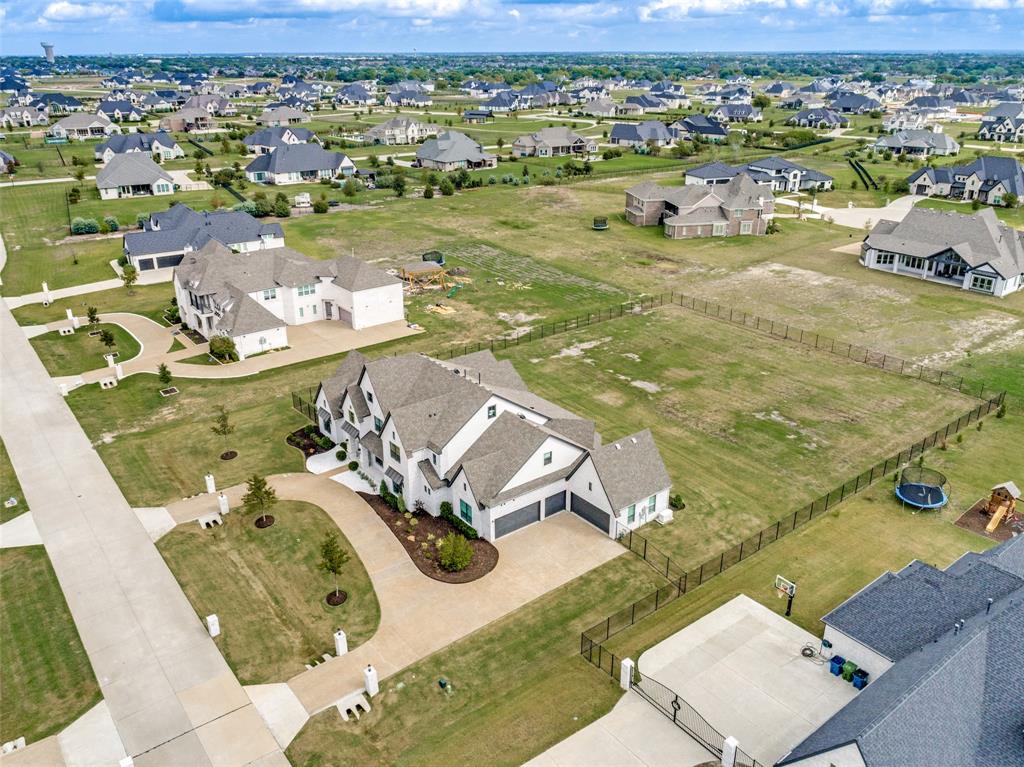 Aerial perspective of a multi-gabled residence featuring a concrete driveway, attached multi-car garage, and a sprawling, fenced lot