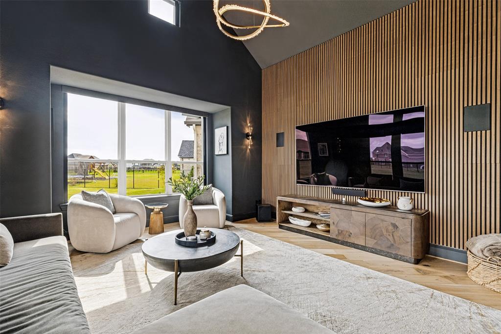 Vaulted ceiling, vertical wood slat accent wall, large picture window, and wide-plank wood-finish flooring