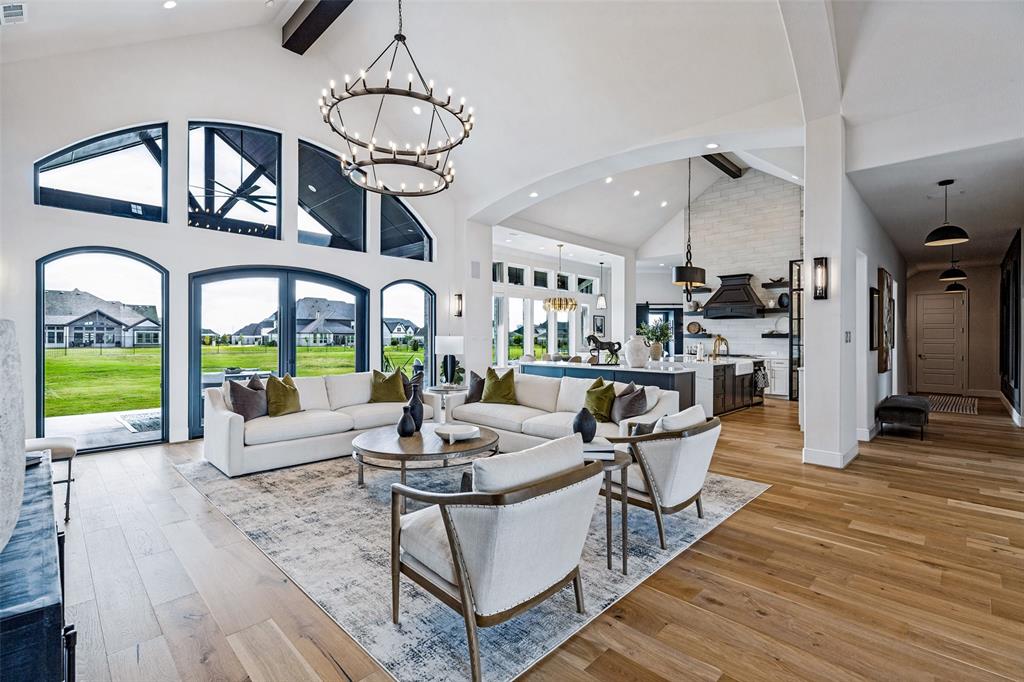 Vaulted ceilings with exposed timber beams, expansive arched windows, wide-plank wood-finish flooring, custom iron chandelier, and a floor-to-ceiling masonry fireplace facade Vaulted ceilings with exposed timber beams, expansive arched windows, wide-plank wood-finish flooring, custom iron chandelier, and a floor-to-ceiling masonry fireplace facade