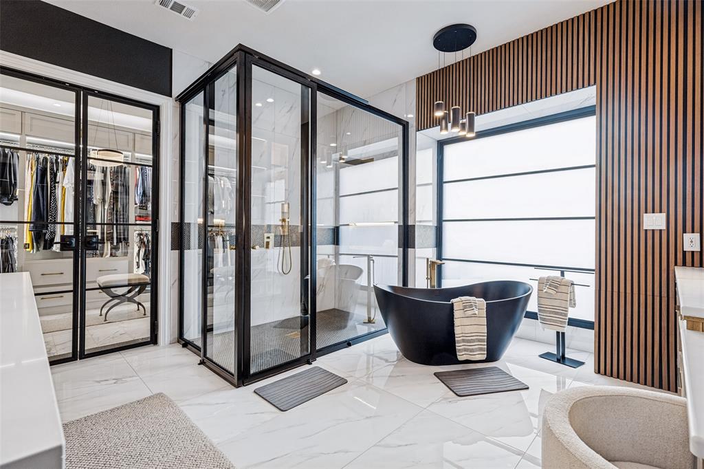 Enclosed glass shower with black metal framing, matte black freestanding soaking tub, vertical wood-slat accent wall, and large-format tile flooring
