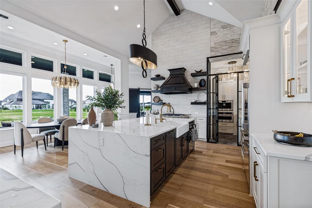 Kitchen featuring a vaulted ceiling with a stacked-stone accent wall, expansive quartz waterfall island, custom matte black cabinetry, and wood-finish flooring