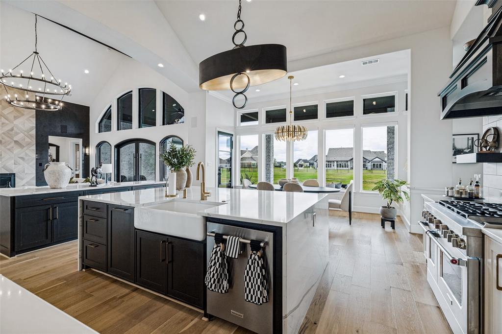 Kitchen featuring a large central island with quartz countertops and a farmhouse-style apron sink, custom dark cabinetry, high-end stainless steel range, and wood-finish flooring under vaulted ceilings