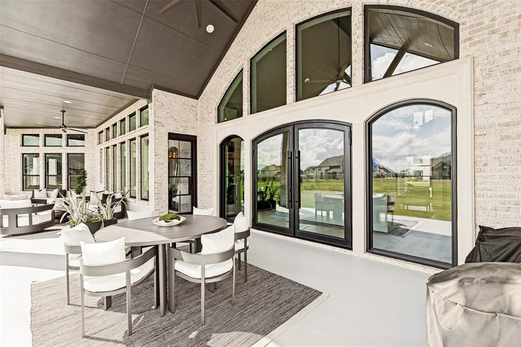 Covered patio featuring white brick exterior walls, dark-framed arched glass double doors, expansive fixed-pane arched transom windows, and a vaulted ceiling with integrated recessed lighting