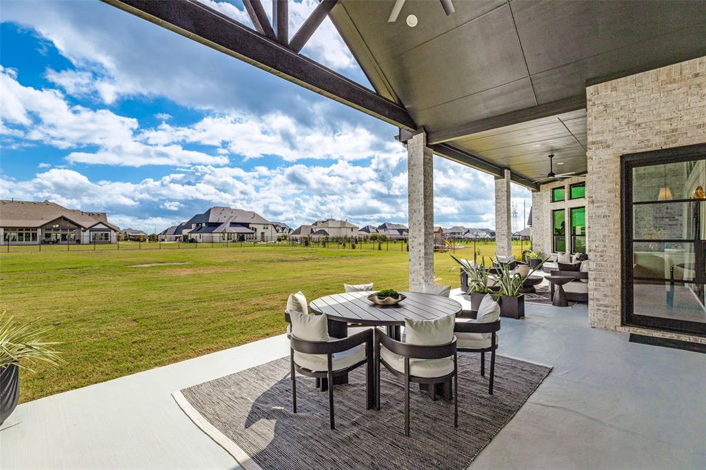 Covered rear patio featuring a vaulted ceiling with exposed timber beams, brick column supports, concrete flooring, and multi-pane black-trimmed glass doors
