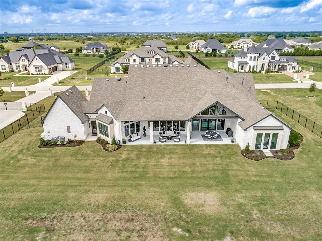 Aerial perspective of a multi-gabled residence featuring a light-colored brick exterior, expansive rear covered patio, large windows, and an encompassing fence