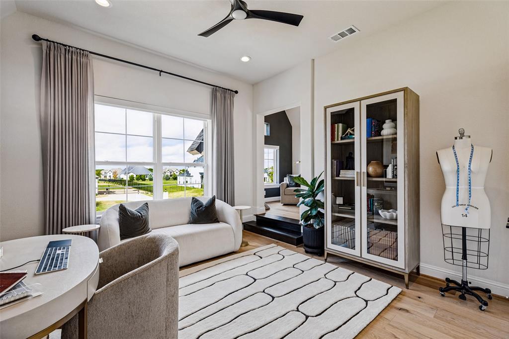 Room featuring wood-finish flooring, high ceilings, large multi-pane windows, and a black matte ceiling fan