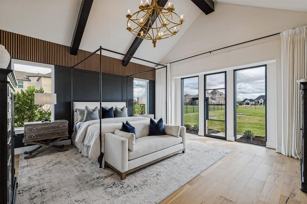 Vaulted ceiling with exposed dark wood beams, vertical slat wood accent wall, floor-to-ceiling multi-panel windows with black frames, brass-finish tiered chandelier, and light wood-finish flooring