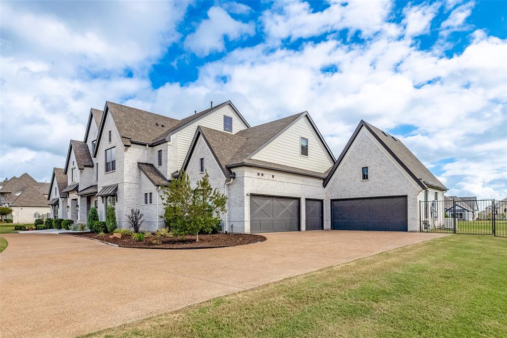 Multi-gabled exterior featuring light-toned brick masonry, horizontal siding accents, a five-car garage with dark carriage-style doors, and an expansive stamped concrete driveway Multi-gabled exterior featuring light-toned brick masonry, horizontal siding accents, a five-car garage with dark carriage-style doors, and an expansive stamped concrete driveway