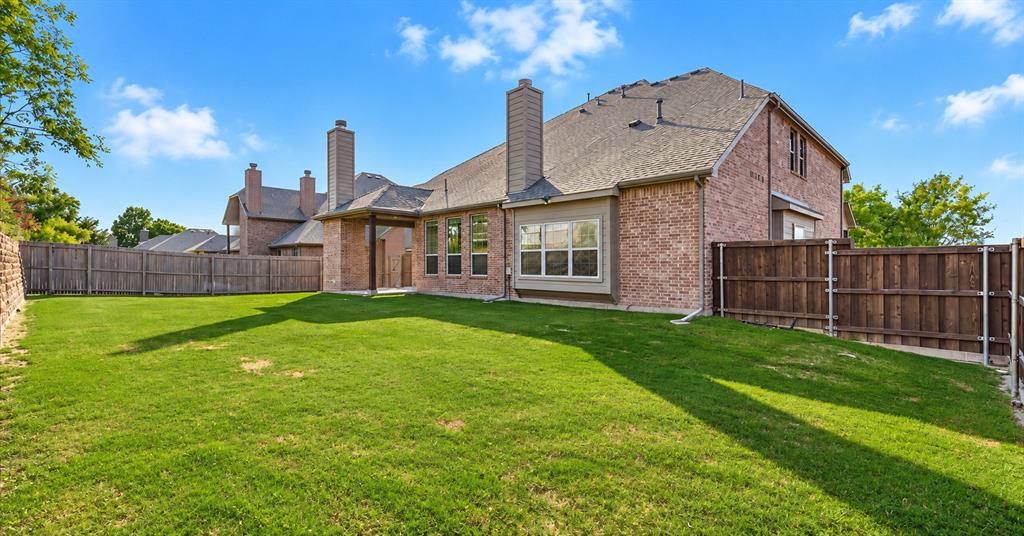 Brick exterior with dual masonry chimneys, covered patio, and fenced backyard featuring a manicured lawn