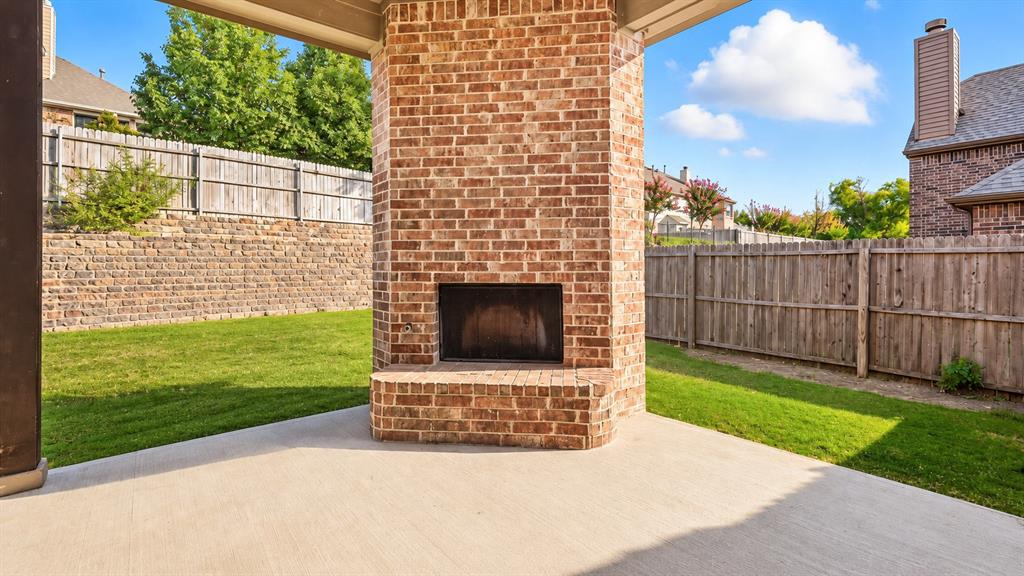 Covered patio featuring a floor-to-ceiling brick fireplace with a raised hearth, concrete flooring, and an enclosed backyard with wood fencing