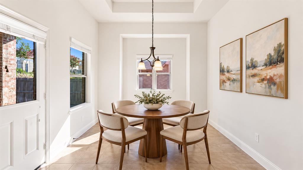 Tray ceiling, three-light metal pendant fixture, tile flooring, and multiple windows with integrated blinds