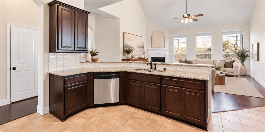 Kitchen featuring dark wood cabinetry, stone countertops, stainless steel dishwasher, vaulted ceiling, and fireplace