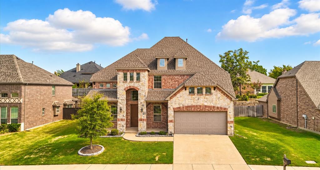 Multi-story residence featuring a brick and stone facade, a multi-gabled roofline, dormer windows, and an attached two-car garage Multi-story residence featuring a brick and stone facade, a multi-gabled roofline, dormer windows, and an attached two-car garage