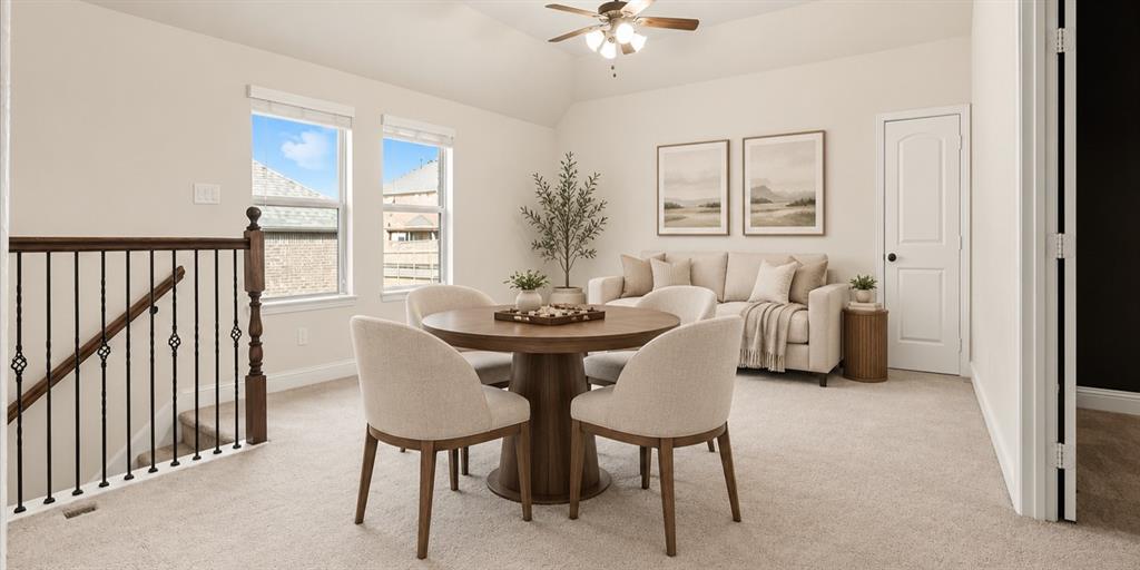 Vaulted ceiling with an integrated light-and-fan fixture, carpeted flooring, two paneled windows, and a black wrought-iron stair railing with a wooden newel post