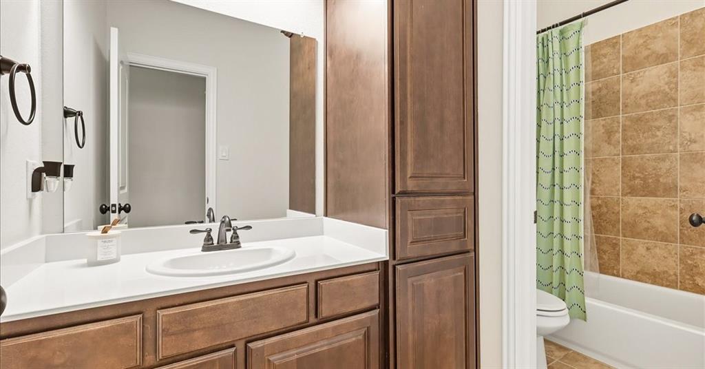 Bathroom vanity featuring stained wood cabinetry, a white countertop with an integrated oval sink, matte black hardware, and an expansive wall-mounted mirror