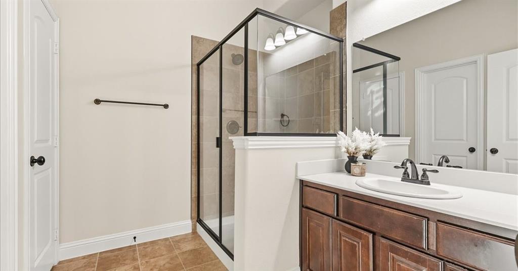 Bathroom featuring a walk-in shower with black-finish framing, neutral tile surround, vanity with cabinetry, solid-surface countertop, and an integrated oval sink