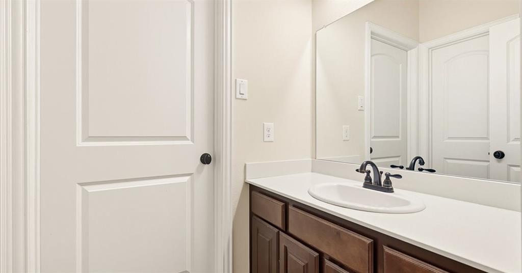 Bathroom vanity featuring dark-stained wood cabinetry, a solid-surface countertop with an integrated oval sink, a matte-finish dark faucet, and a large wall-mounted mirror