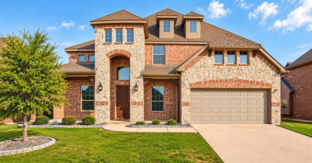 Two-story exterior featuring a brick and stone facade, arched entryway, dormer windows, and a multi-car garage