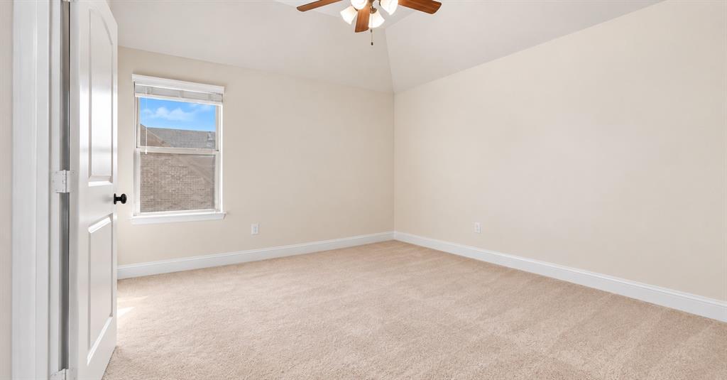 Neutral-toned room featuring a vaulted ceiling, textured carpet, single-pane window, and a central ceiling fan with integrated light fixture
