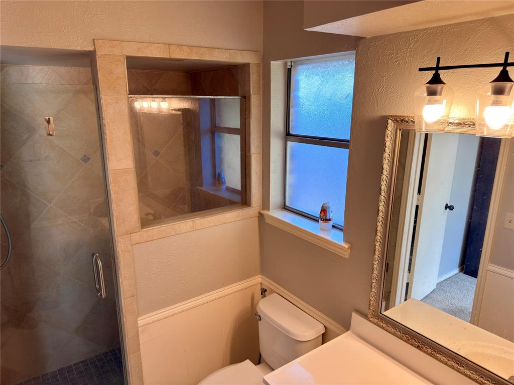 Walk-in shower with tile surround, glass enclosure, opaque window, and dual-bulb wall-mounted vanity lighting