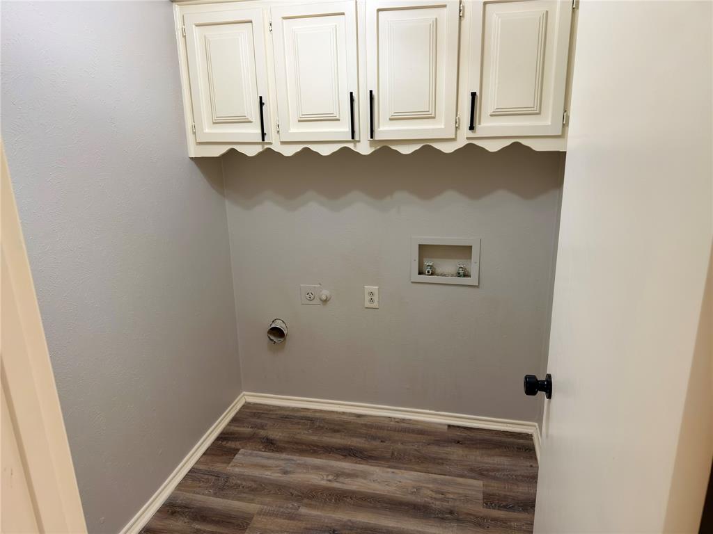Laundry area featuring wood-finish flooring, white wall-mounted cabinetry with scalloped detailing, and matte black hardware Laundry area featuring wood-finish flooring, white wall-mounted cabinetry with scalloped detailing, and matte black hardware