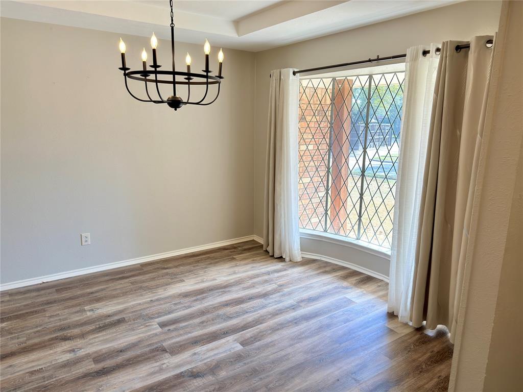 Wood-finish flooring, tray ceiling, multi-light iron chandelier, and diamond-patterned window pane insert