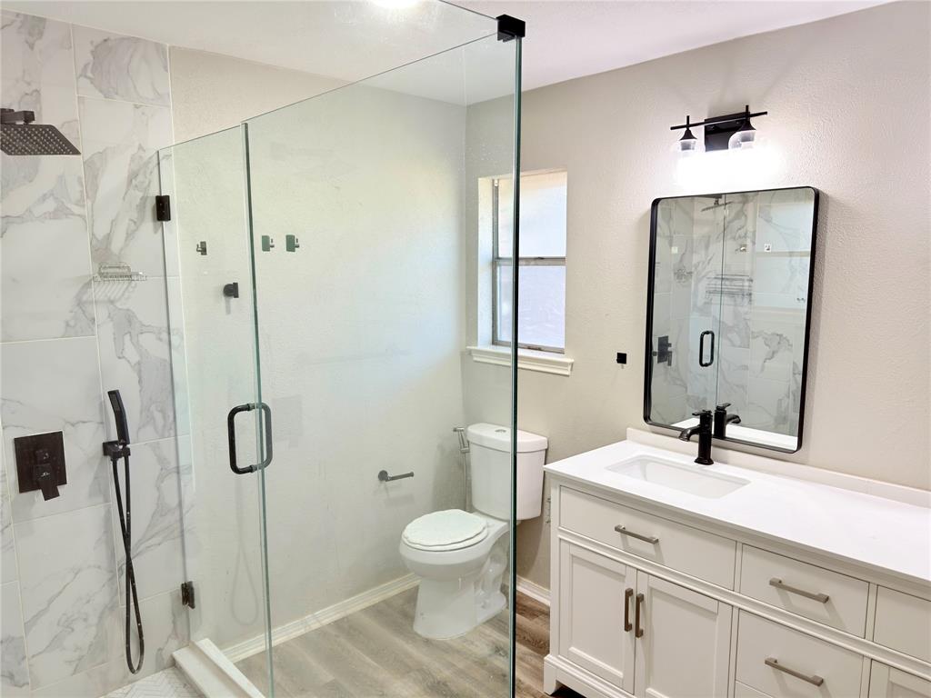 Bathroom featuring a frameless glass-enclosed shower with large-format tile surround, rainfall showerhead, and handheld sprayer Bathroom featuring a frameless glass-enclosed shower with large-format tile surround, rainfall showerhead, and handheld sprayer