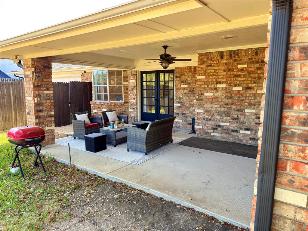 Covered patio featuring a concrete slab, exterior brick wall, built-in ceiling fan, and double-door entrance
