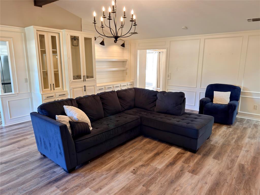 Built-in cabinetry featuring glass-front display doors, wood-finish flooring, custom wall molding, open floating shelving, and a multi-arm chandelier
