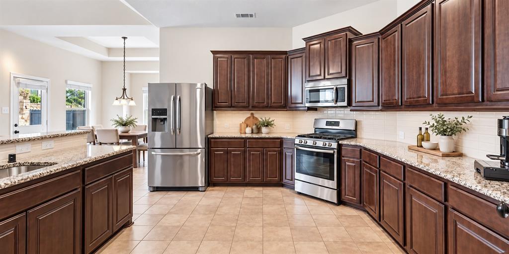 Kitchen featuring stained wood cabinetry, stone countertops, tiled backsplash, stainless steel appliances, and ceramic tile flooring