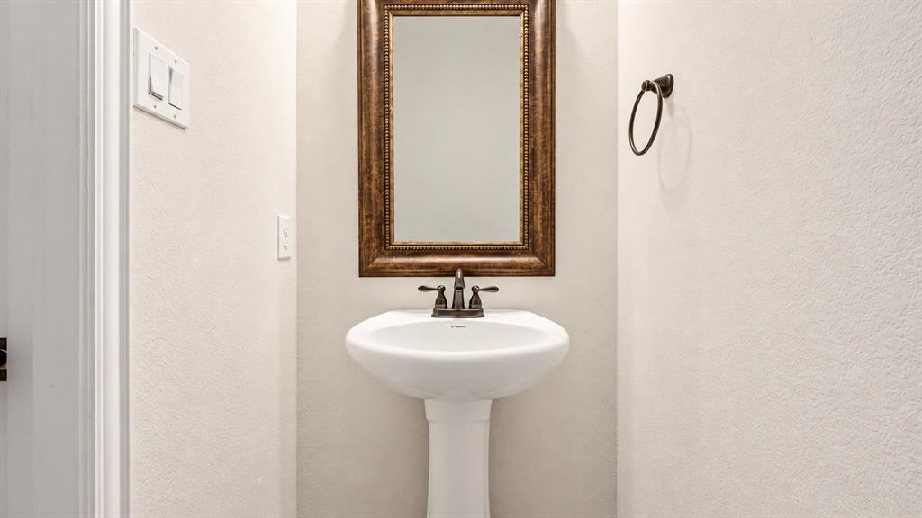 White pedestal sink with a dual-handle bronze faucet, complemented by a framed rectangular mirror and a matching bronze towel ring