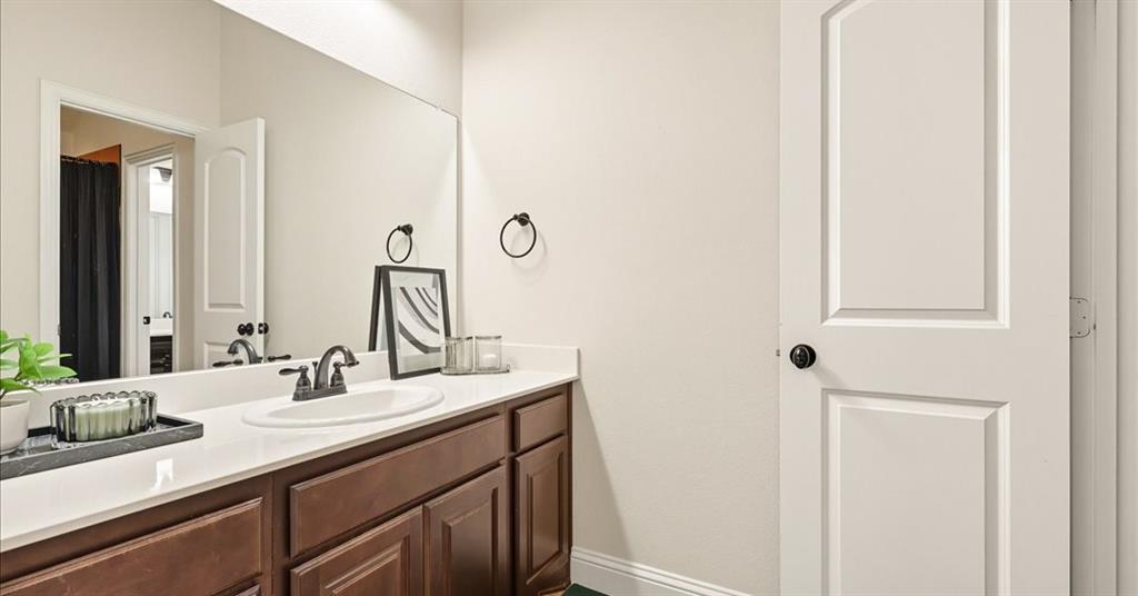 Bathroom featuring dark wood cabinetry, a light-toned countertop with an integrated basin, a widespread faucet, a large vanity mirror, and a two-panel interior door