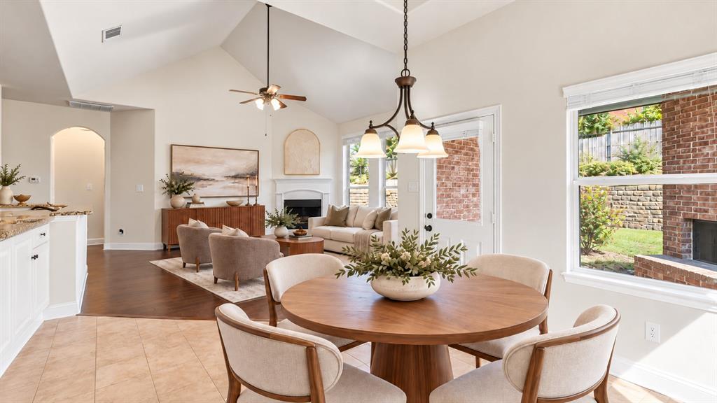 Vaulted ceilings featuring a chandelier and ceiling fan, wood-finish flooring, a fireplace with a white mantel, and a multi-pane glass door