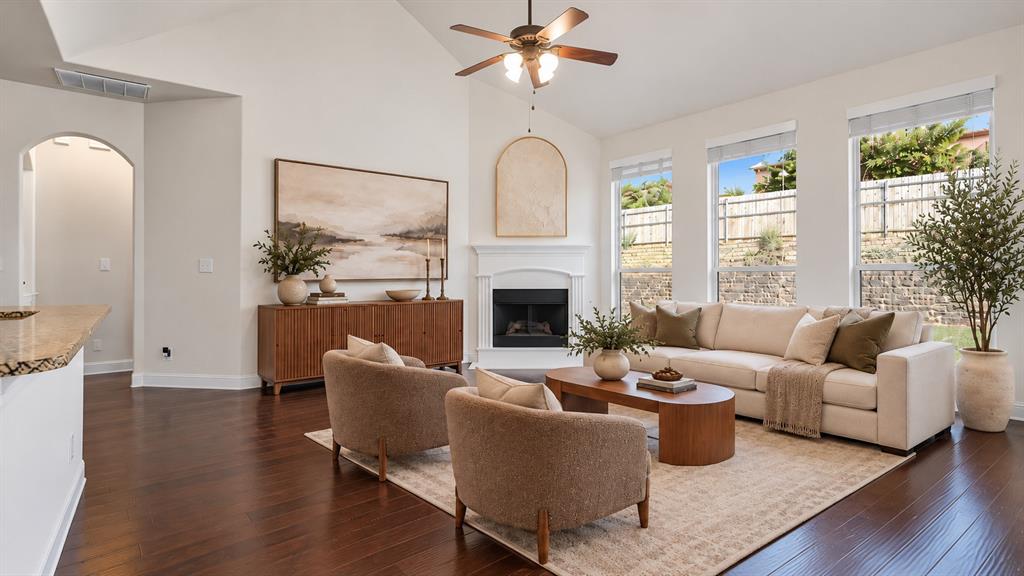 Living area featuring vaulted ceilings, wood-finish flooring, corner fireplace with a white mantel, and large windows