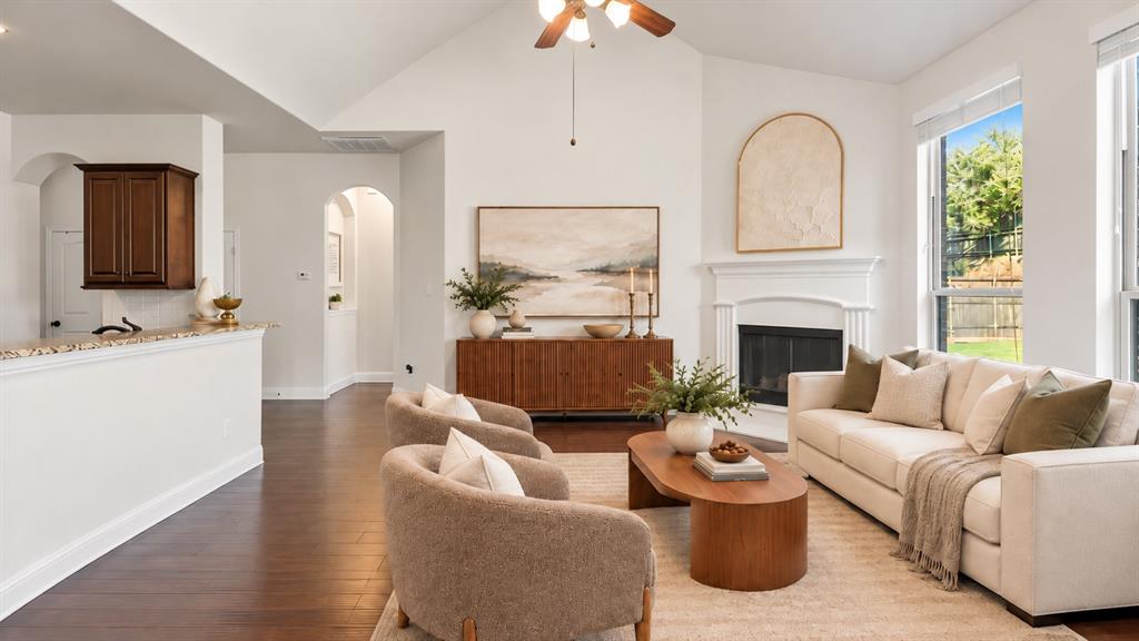 Vaulted ceiling, wood-finish flooring, fireplace with a decorative mantel, and multi-paned windows
